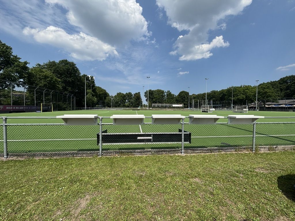 Een rij Veldbarren langs de lijn van het hockeyveld onder een wolkenlucht