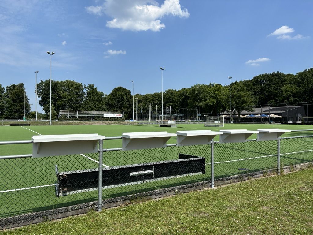 Vijf Veldbarren naast elkaar aan het hek van het hockeyveld